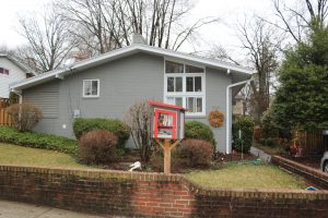 A gray and white house, with a little free library out front.